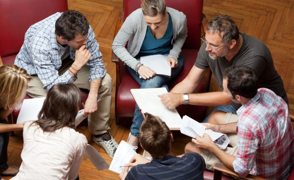 Gruppo di adulti che studiano e discutono insieme seduti in cerchio, rappresentando l'approccio multidisciplinare di Superprof