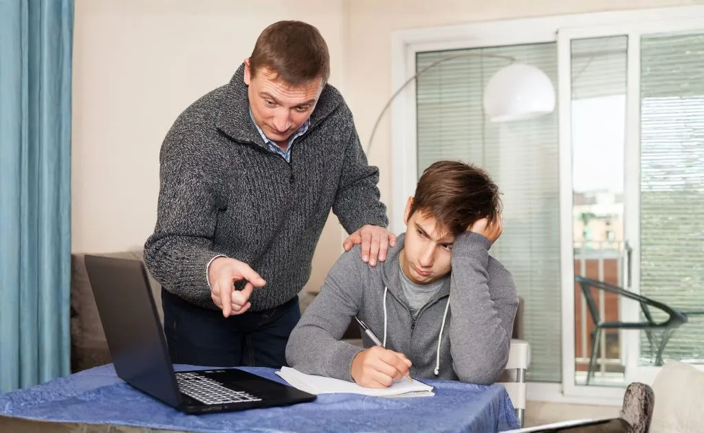 Padre che aiuta il figlio adolescente svogliato a studiare al laptop a casa