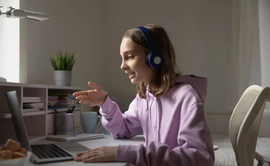 Ragazza con cuffie che segue una lezione di ripetizioni online al laptop da casa
