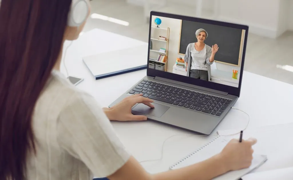 Studentessa con cuffie che segue una lezione online con il suo insegnante al laptop da casa